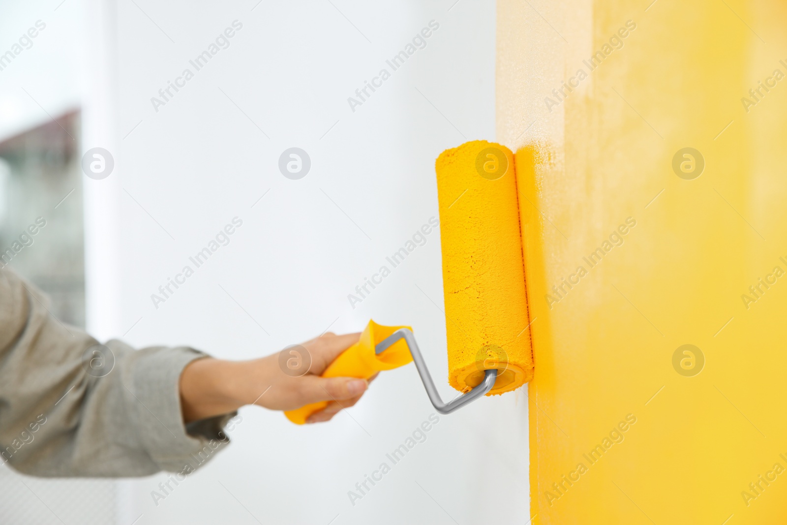 Photo of Woman painting white wall with yellow dye, closeup. Interior renovation