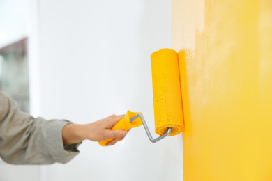 Photo of Woman painting white wall with yellow dye, closeup. Interior renovation