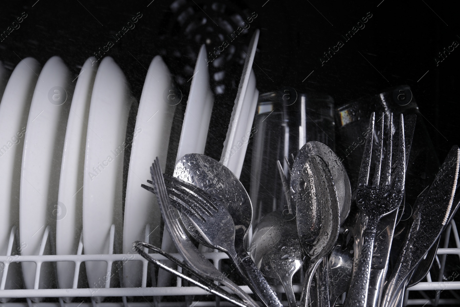 Photo of Clean wet plates and cutlery in dishwasher, closeup