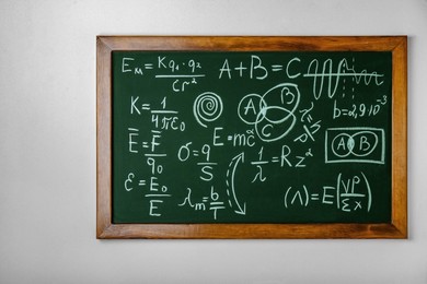 Blackboard with different physical formulas written with chalk on white wall