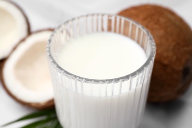 Glass of delicious coconut milk, palm leaf and coconuts on white table