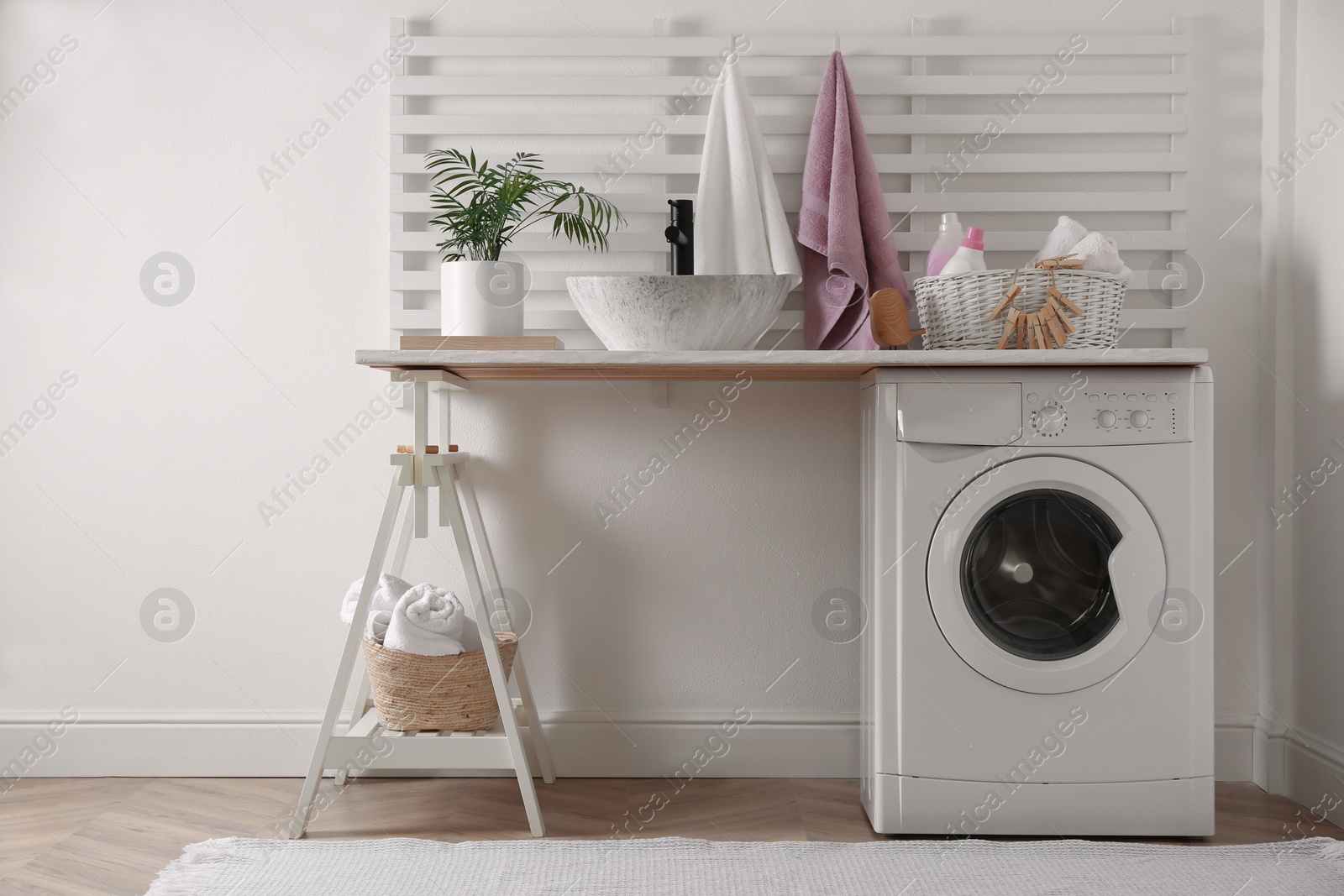 Photo of Laundry room interior with modern washing machine and stylish vessel sink on white wooden countertop