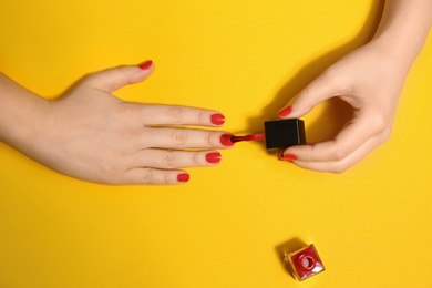 Photo of Woman applying nail polish on color background, top view