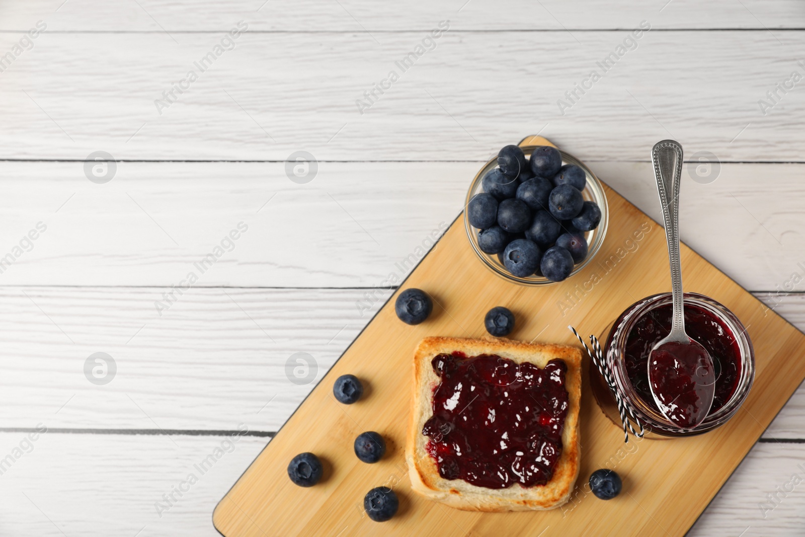 Photo of Delicious toast with blueberry jam and fresh berries on white wooden table, top view. Space for text