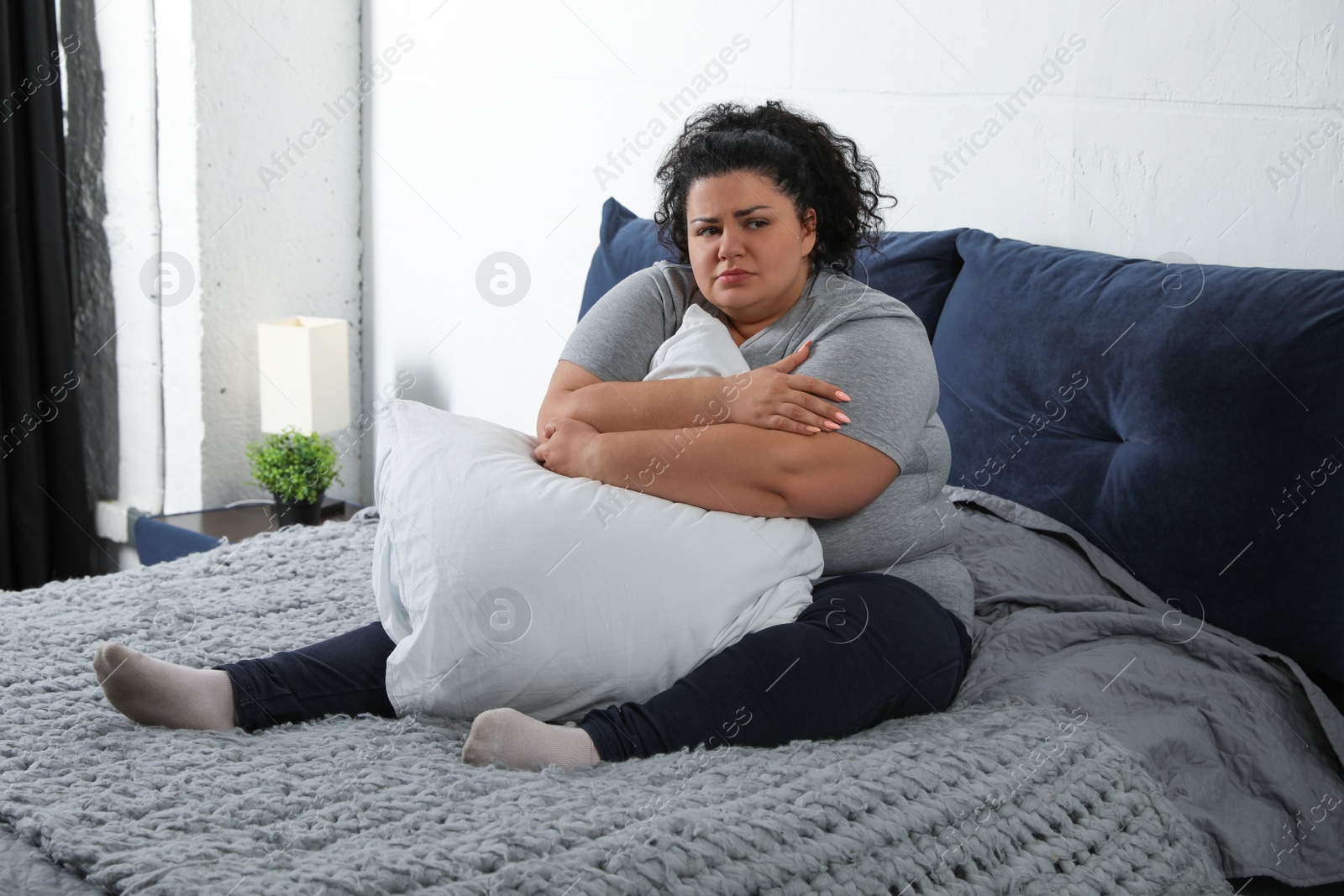 Photo of Depressed overweight woman hugging pillow on bed