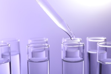 Dripping liquid from pipette into test tube on violet background, closeup