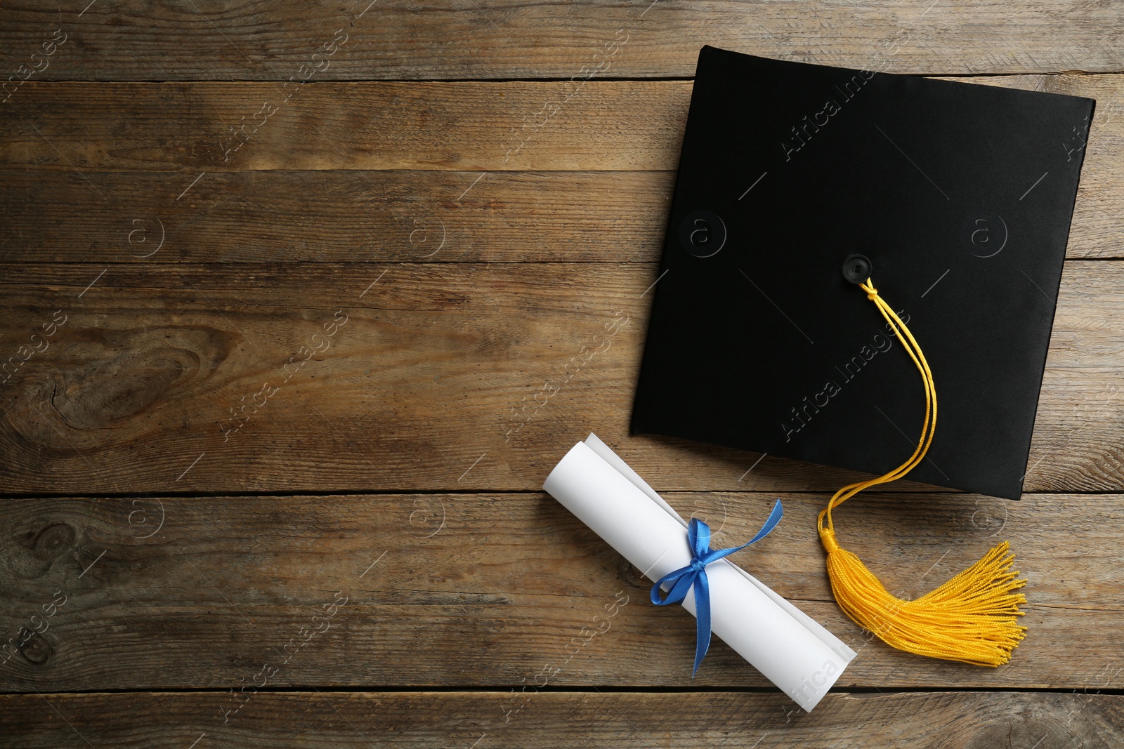 Photo of Graduation hat and diploma on wooden table, flat lay. Space for text