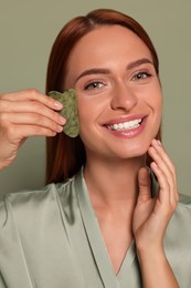 Photo of Young woman massaging her face with jade gua sha tool on green background
