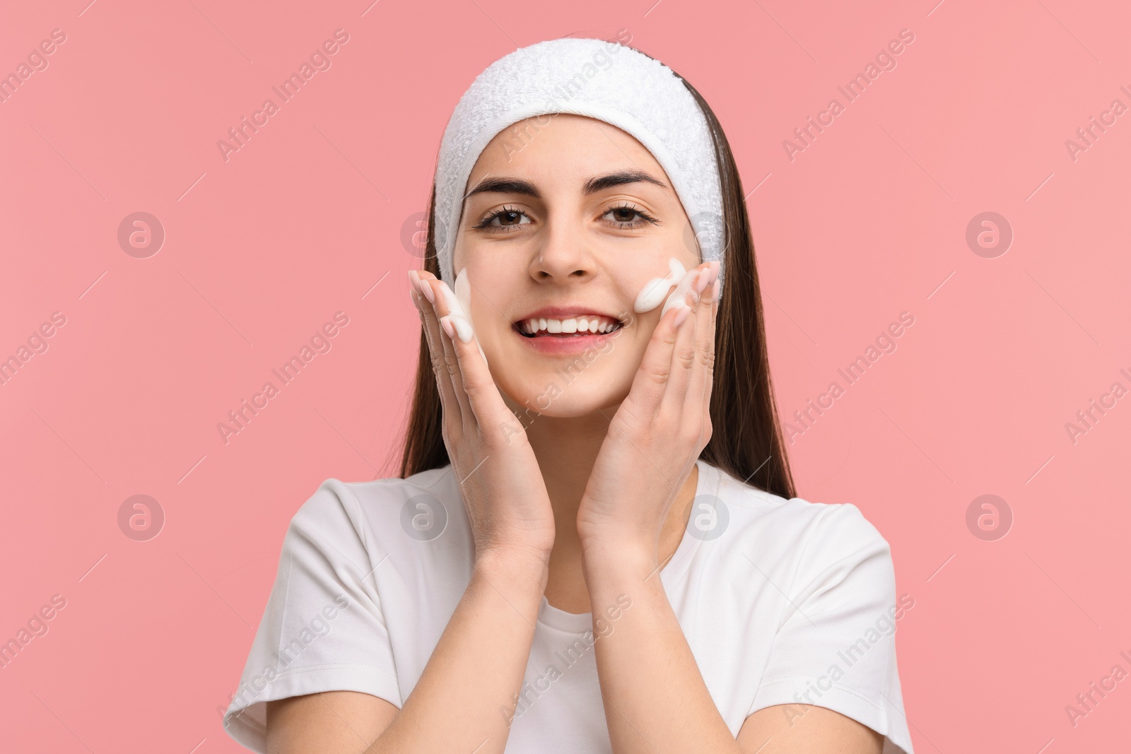 Photo of Young woman with headband washing her face on pink background