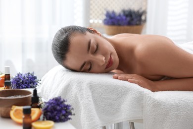 Photo of Beautiful young woman relaxing on massage couch and bottles of essential oil with ingredients on table in spa salon