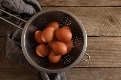 Chicken eggs in colander and napkin on wooden table, top view