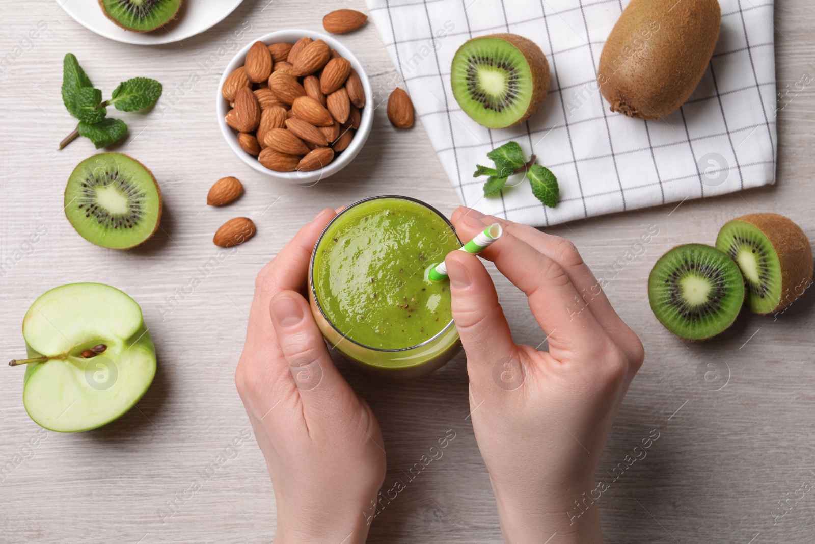 Photo of Woman with delicious kiwi smoothie and ingredients at white wooden table, top view