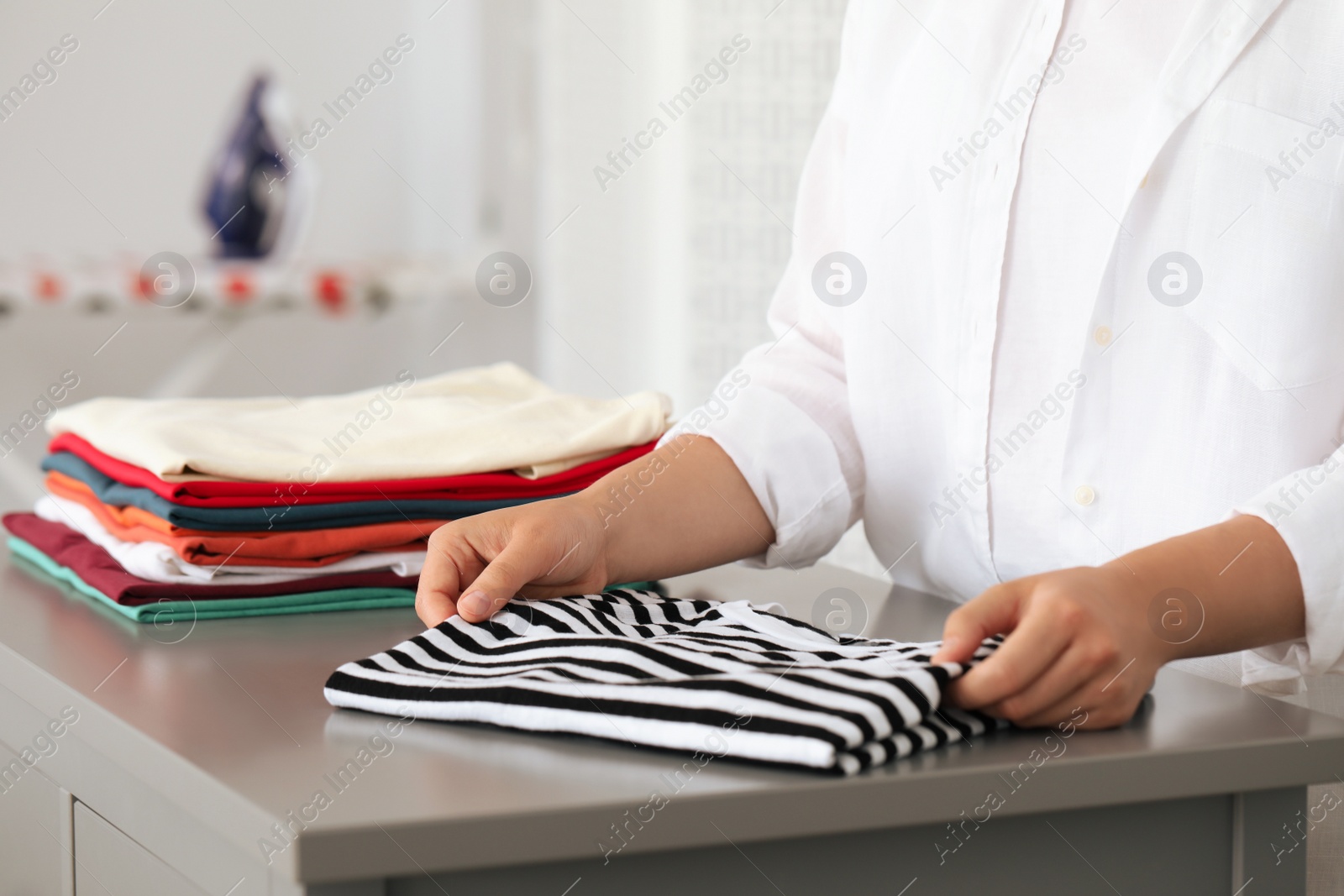 Photo of Woman folding clothes at grey table indoors, closeup