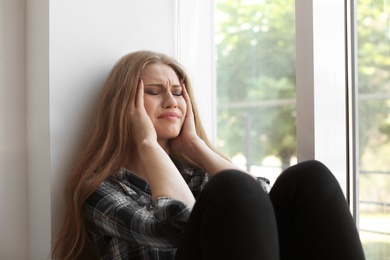 Photo of Depressed young woman sitting near window