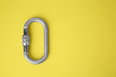 One metal carabiner on yellow background, top view. Space for text