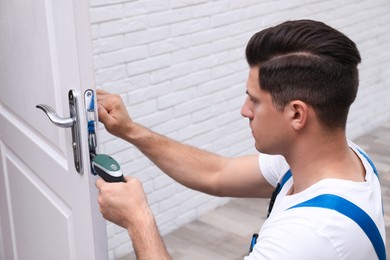 Photo of Handyman with screw gun repairing door lock indoors
