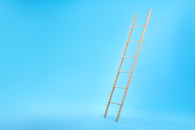Photo of Modern wooden ladder on light blue background. Space for text