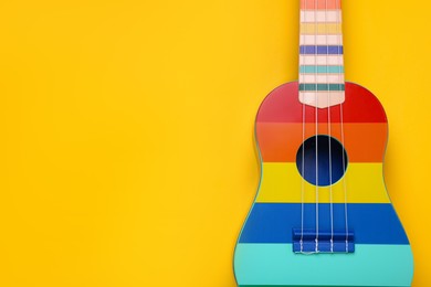 Photo of Colorful ukulele on yellow background, top view with space for text. String musical instrument