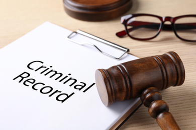 Image of Clipboard with words CRIMINAL RECORD and gavel on wooden table, closeup