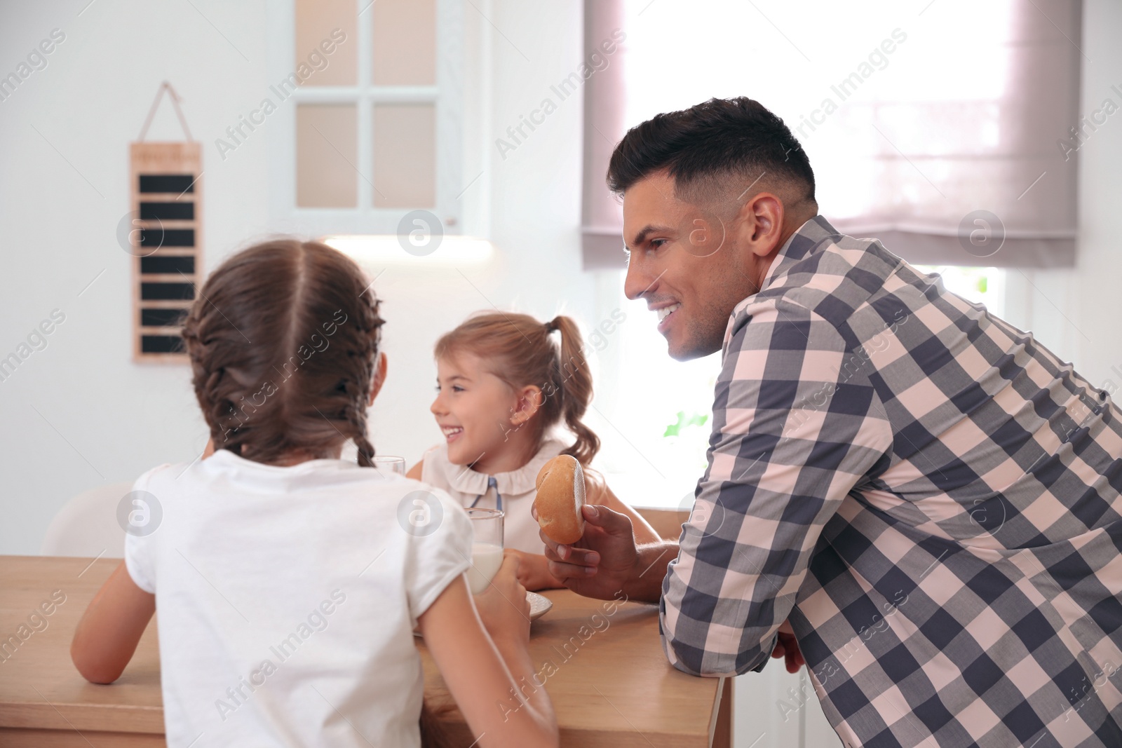 Photo of Little girls and their father eating together at table in modern kitchen