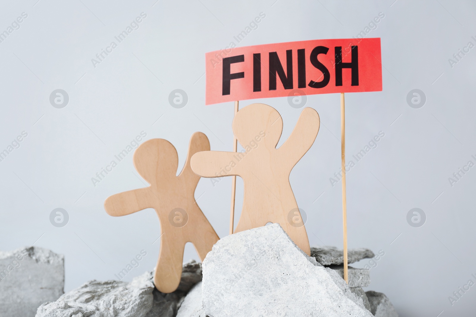 Photo of Competition concept. Wooden human figures on stones and red sign with word Finish against grey background