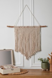 Photo of Open jewelry box and decor elements on wooden table near white wall with stylish macrame