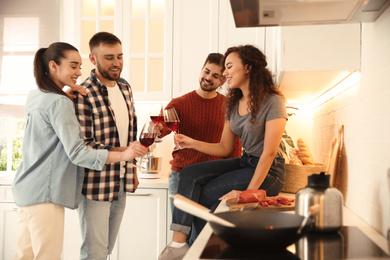 Photo of Happy people drinking wine while cooking food in kitchen