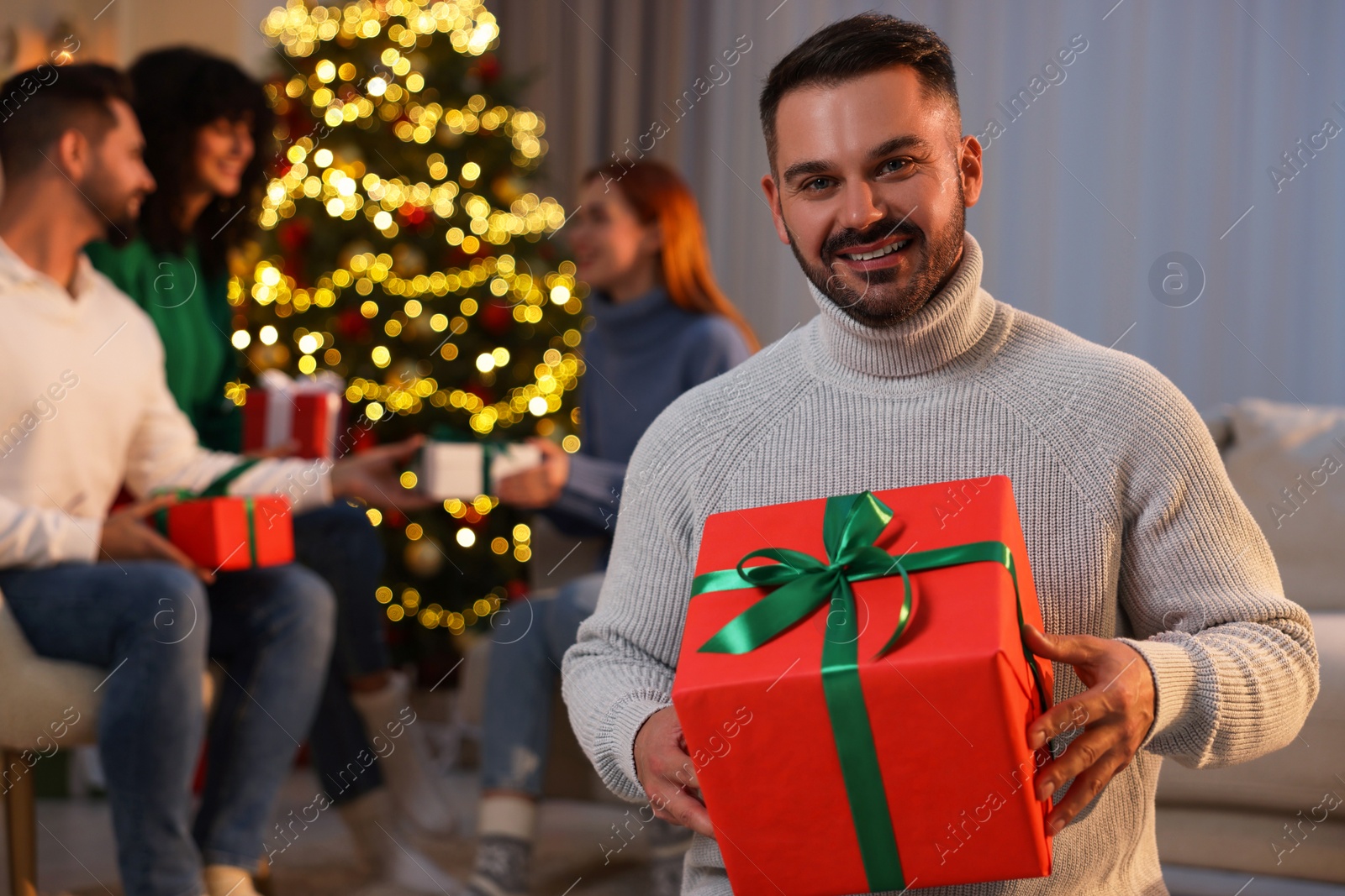 Photo of Christmas celebration in circle of friends. Happy man with gift box at home, selective focus