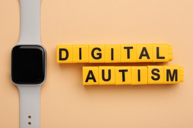 Photo of Phrase Digital Autism made of yellow cubes and smartwatch on beige background, flat lay. Addictive behavior