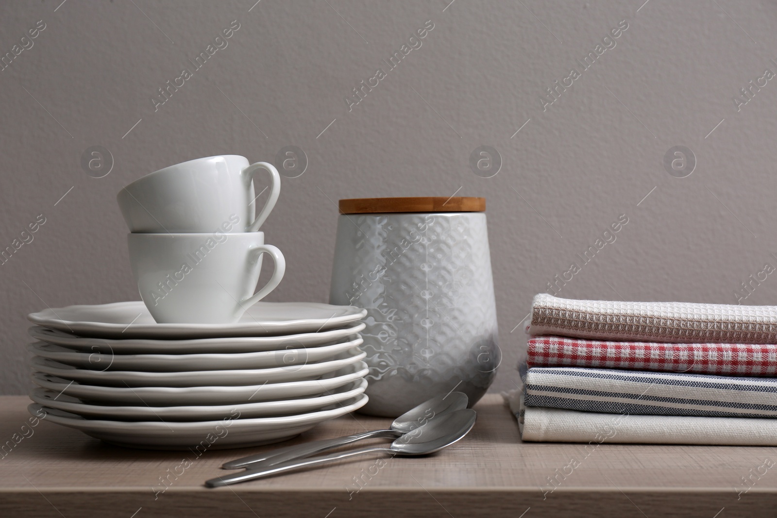 Photo of Stack of soft kitchen towels and dishware on wooden table against grey background