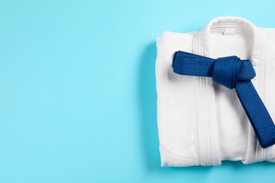 Photo of Karate belt and white kimono on light blue background, top view. Space for text