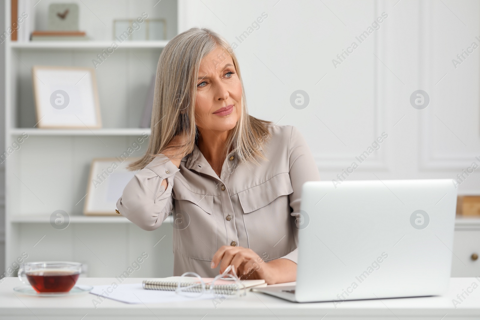 Photo of Woman suffering from neck pain at workplace in room