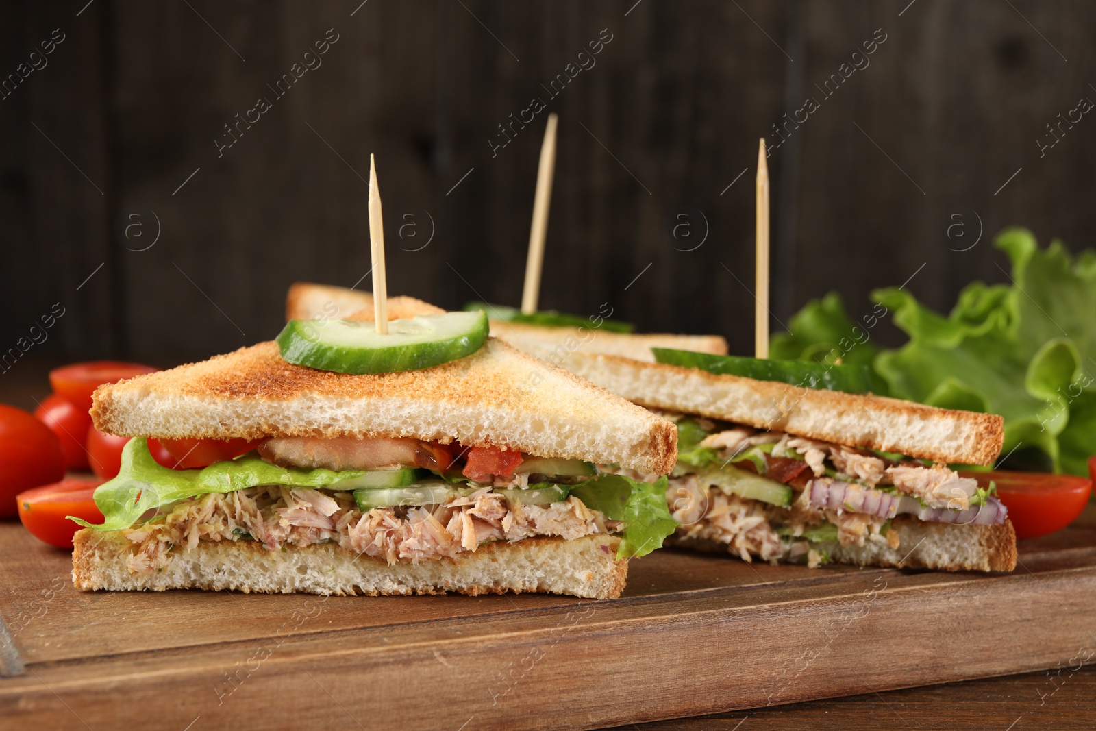 Photo of Delicious sandwiches with tuna and vegetables on wooden board, closeup