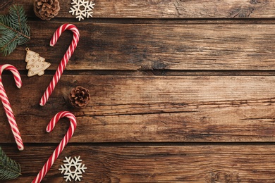 Photo of Flat lay composition with candy canes and Christmas decor on wooden background. Space for text