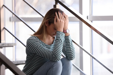 Photo of Emotional teenage girl sitting on stairs indoors