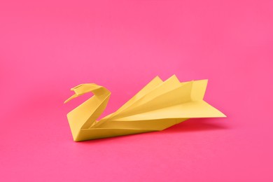 Photo of Yellow paper swan on pink background. Origami art
