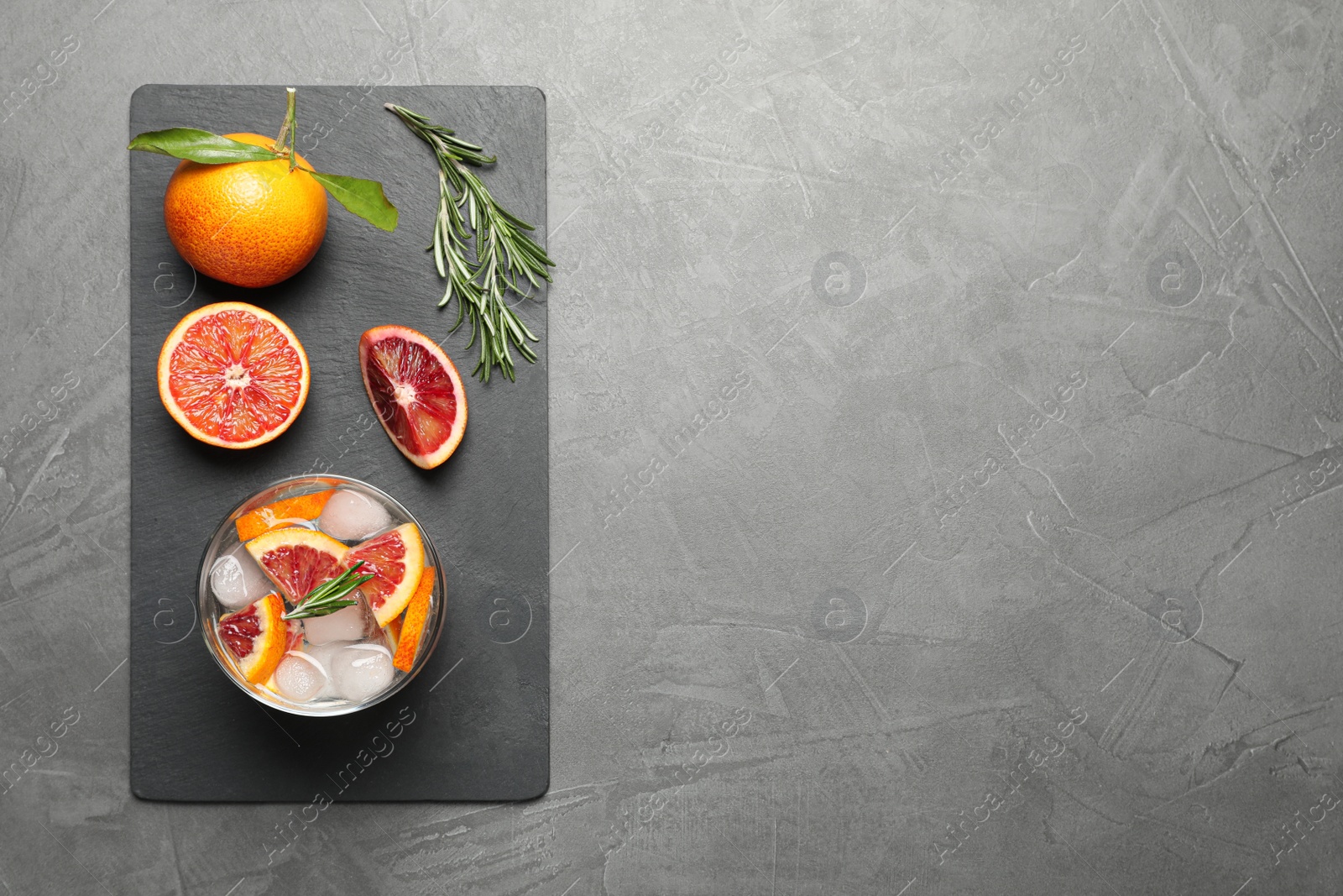 Photo of Delicious refreshing drink with sicilian orange and rosemary near fresh ingredients on grey table, flat lay. Space for text