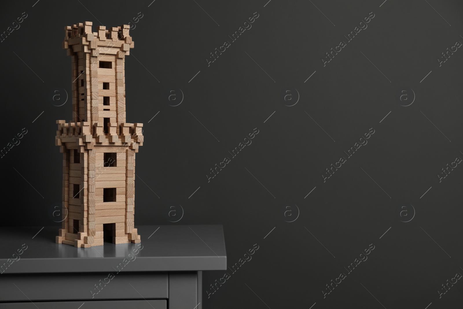 Photo of Wooden tower on chest of drawers near dark grey wall, space for text. Children's toy