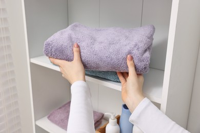 Woman stacking clean towels on shelf indoors, closeup