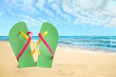 Image of Green flip flops on sandy beach near sea. Space for text 