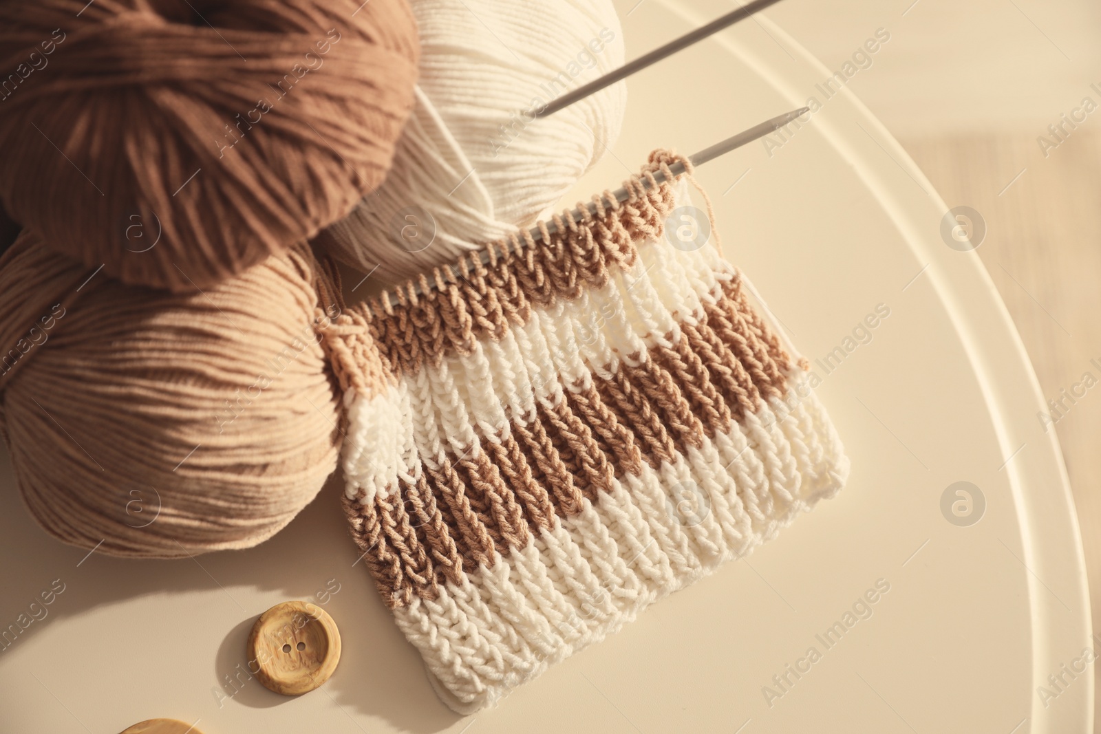 Photo of Yarn balls with knitting needles on white table, top view. Creative hobby