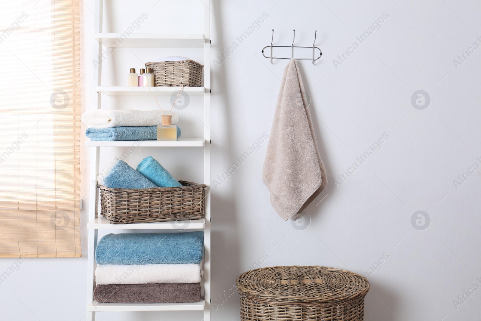 Photo of Shelving unit and rack with clean towels and toiletries near white wall