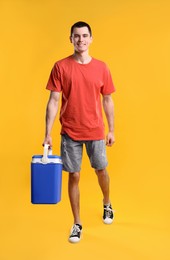 Man with blue cool box walking on orange background