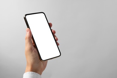 Photo of Man holding smartphone with blank screen on grey background, closeup. Mockup for design