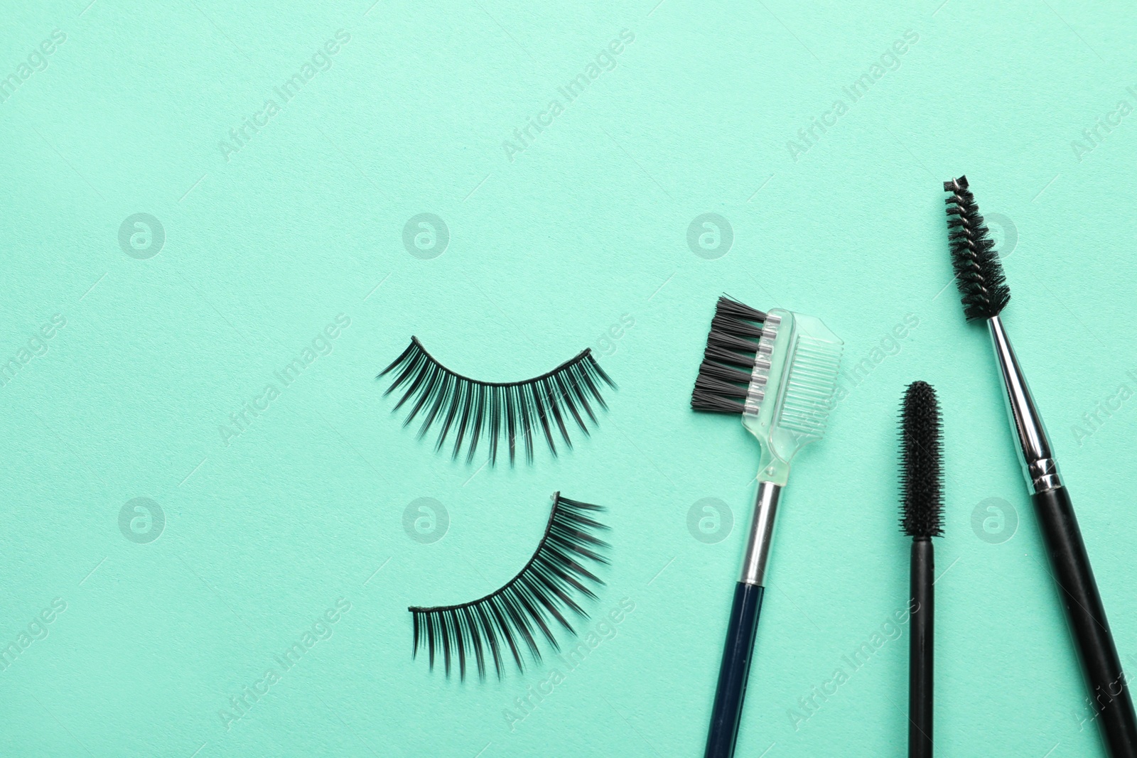 Photo of False eyelashes and brushes on turquoise background, flat lay. Space for text