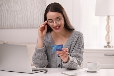 Woman with credit card using laptop for online shopping at white table indoors