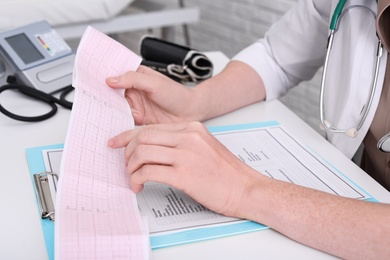 Photo of Doctor examining cardiogram at table in clinic, closeup