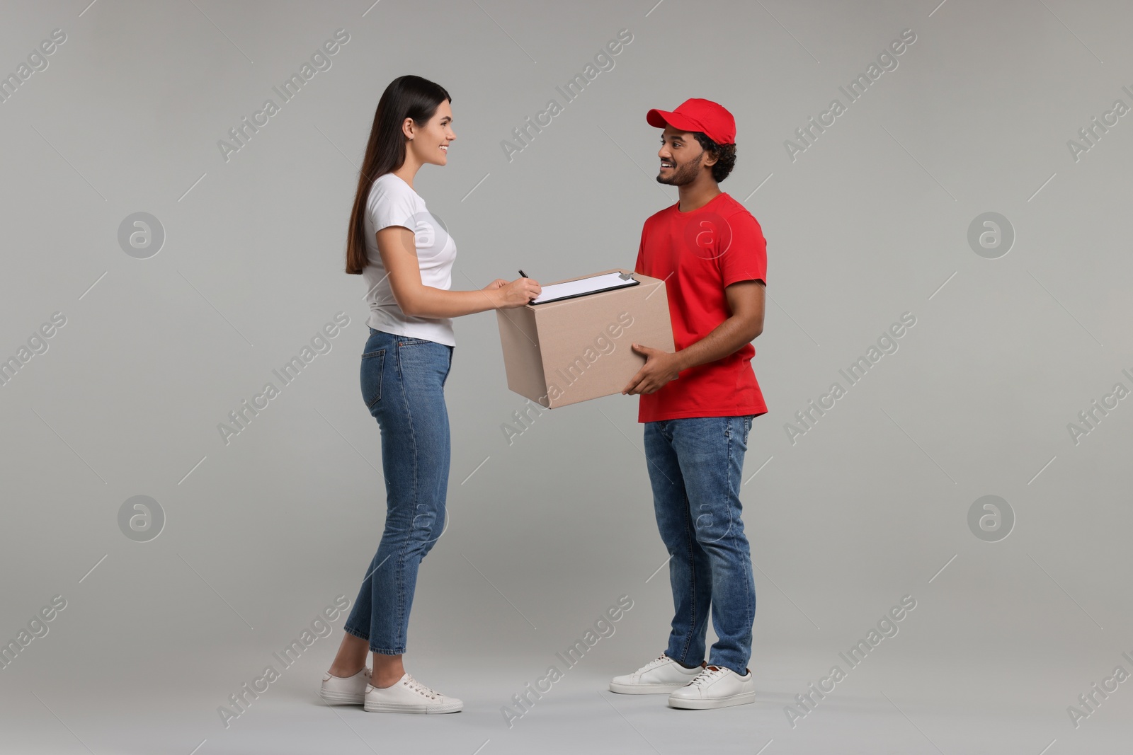 Photo of Smiling woman signing order receipt on grey background. Courier delivery