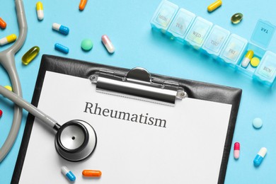 Photo of Clipboard with word Rheumatism, stethoscope and pills on light blue background, flat lay