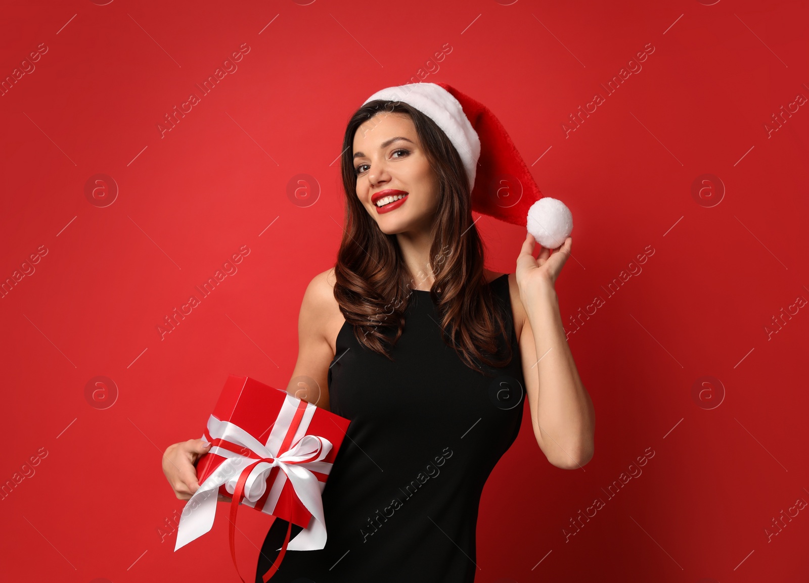 Photo of Beautiful woman wearing Santa hat with Christmas gift on red background